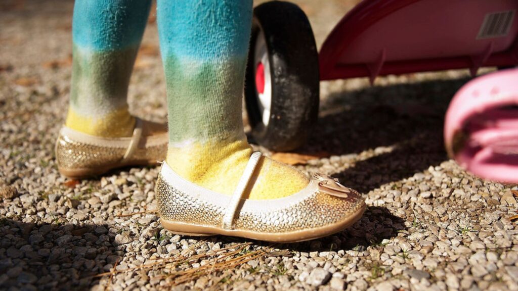 A small child wears tie-dye tights and sparkly, sequin shoes to her family session.